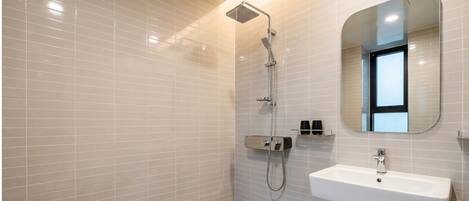 Une salle de bain moderne avec des murs recouverts de carreaux blancs, une douche équipée d’un pommeau de douche à main, un lavabo avec un miroir au-dessus et une petite étagère contenant des articles de toilette.