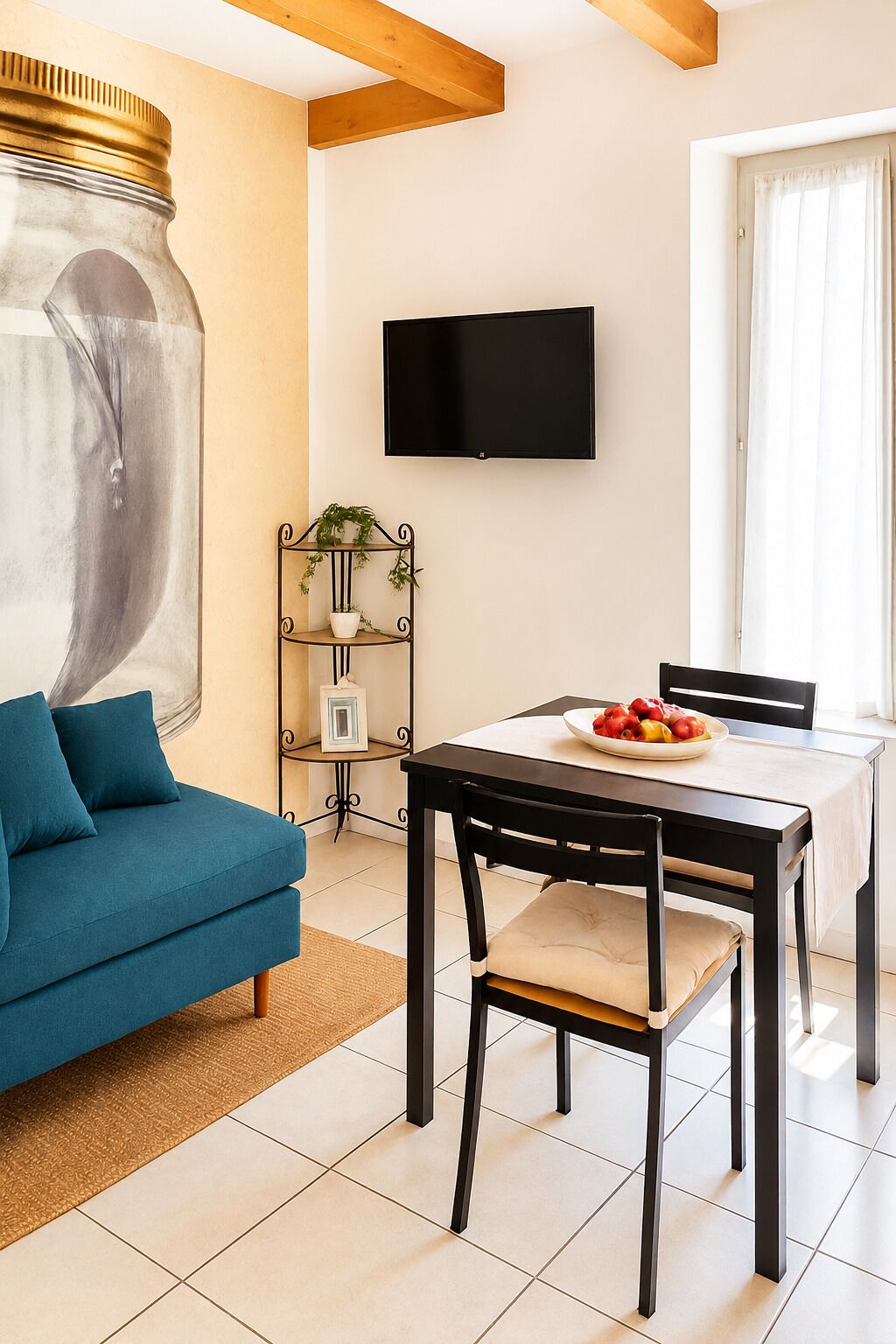 Un saló amb un sofà, una taula de dinar amb cadires, un televisor fixat a la paret i una planta sobre un suport metàl·lic.