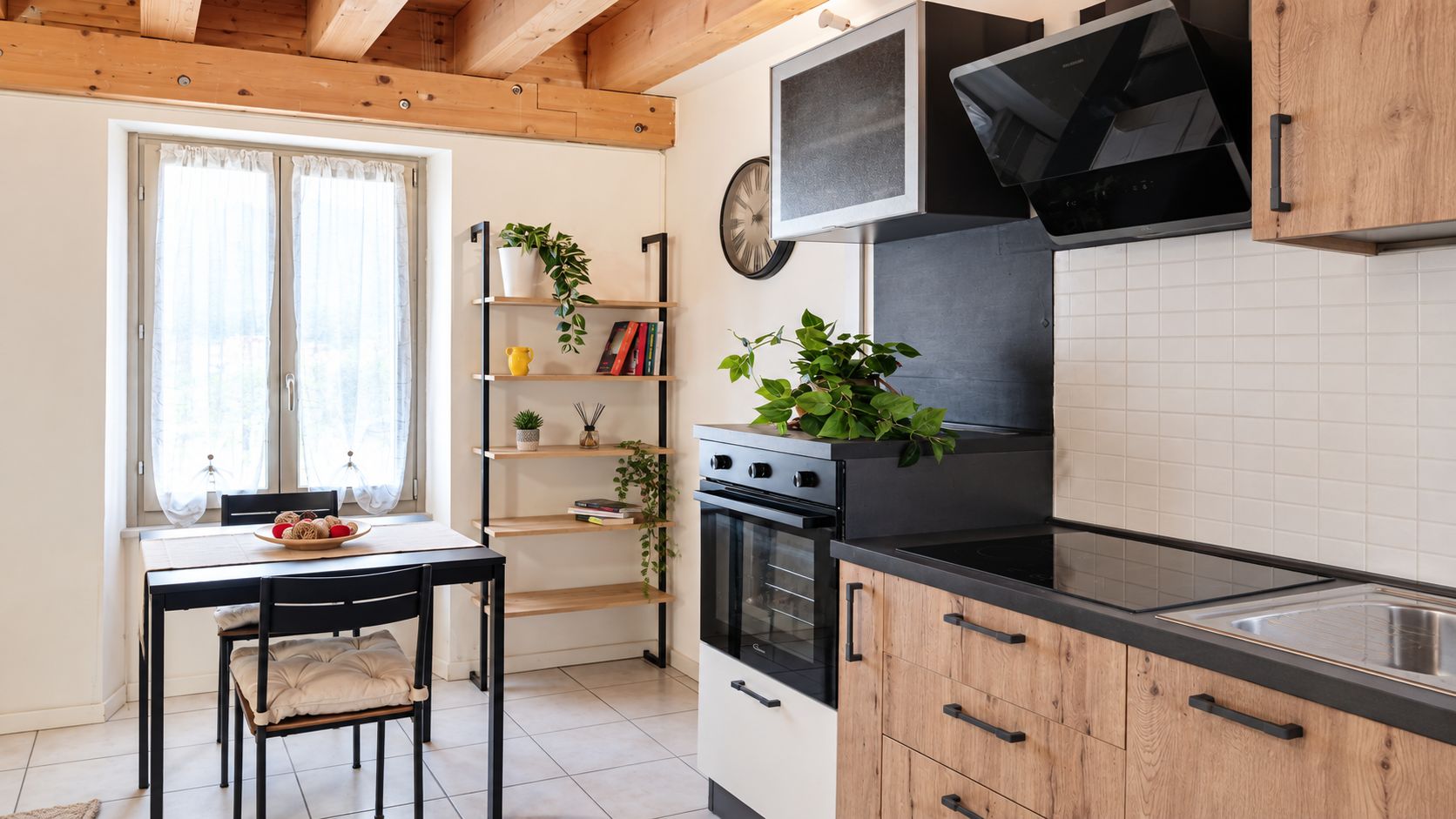 A kitchen with a stove, oven, and black countertop. There is a dining table with chairs and a window with curtains.