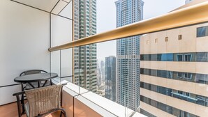 A balcony with a view of tall buildings, a table, and two wicker chairs.
