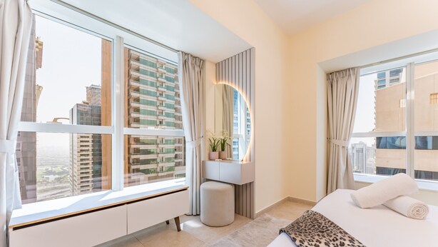 A modern hotel room with a large window, a bed with a leopard print bedspread, a white bedside table, and a small potted plant.