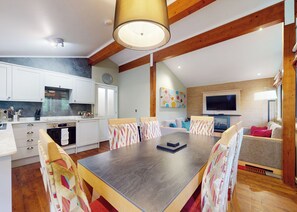 A modern kitchen with white cabinets, a built-in oven, and a dining area with a large table and patterned chairs.