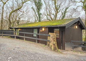 A rustic wooden building with a sloped roof, a wooden fence, and a tree stump in front.