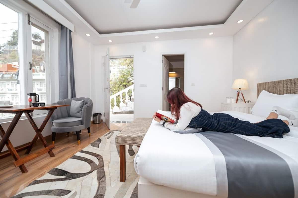 Habitación de hotel con cama, sillón de lectura, una mesita y vistas al exterior.
