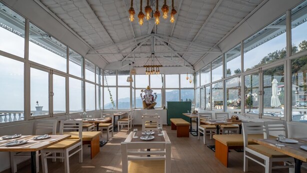 A restaurant with white furniture, large windows, and a view of the sea. - Syona Resort (Mussoorie)