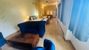 A hotel room with a large bed, a blue sofa, a wooden coffee table, and a desk with a lamp. - Syona Resort (Mussoorie)