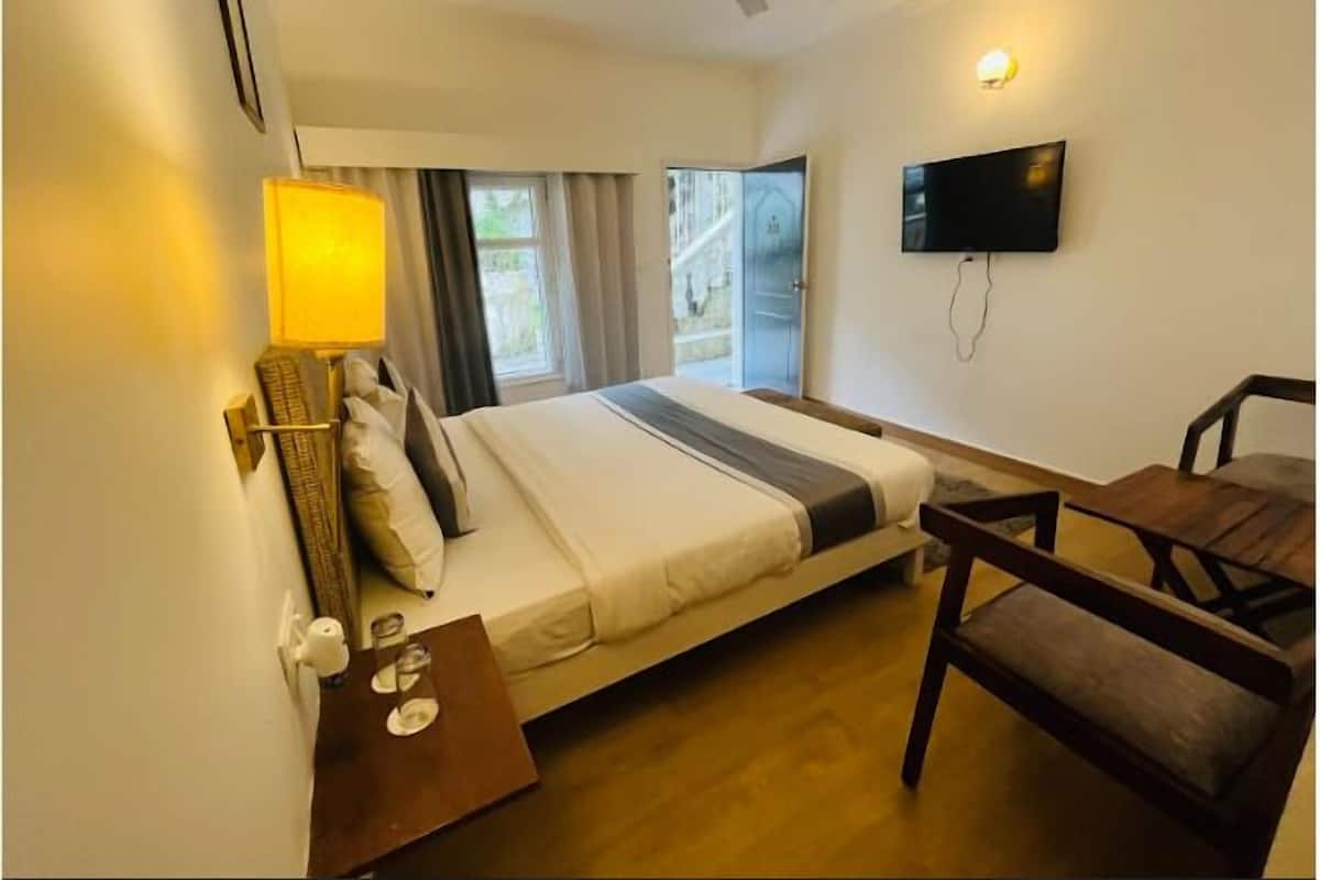 Habitación de hotel con cama, escritorio con lámpara, silla, televisor y ventana con cortinas.