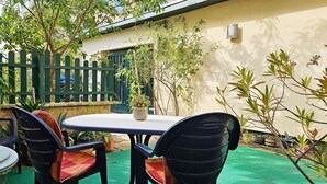 An outdoor patio with a table and chairs, surrounded by plants and a green fence.