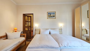 A hotel room with two single beds, a wooden wardrobe, a framed picture on the wall, and a large mirror.