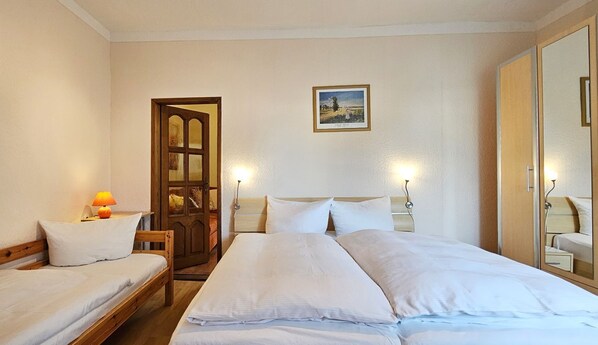 A hotel room with two single beds, a wooden wardrobe, a framed picture on the wall, and a large mirror.
