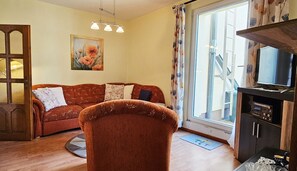 A living room with a sofa, a chair, a television, and a window with curtains.