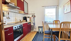 A compact kitchen with red cabinets, a stove, and a dining area with a table and chairs.