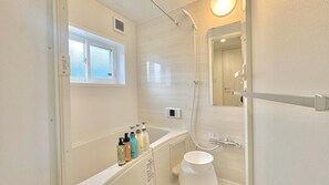 A modern bathroom with a bathtub, shower, and a window above the tub.