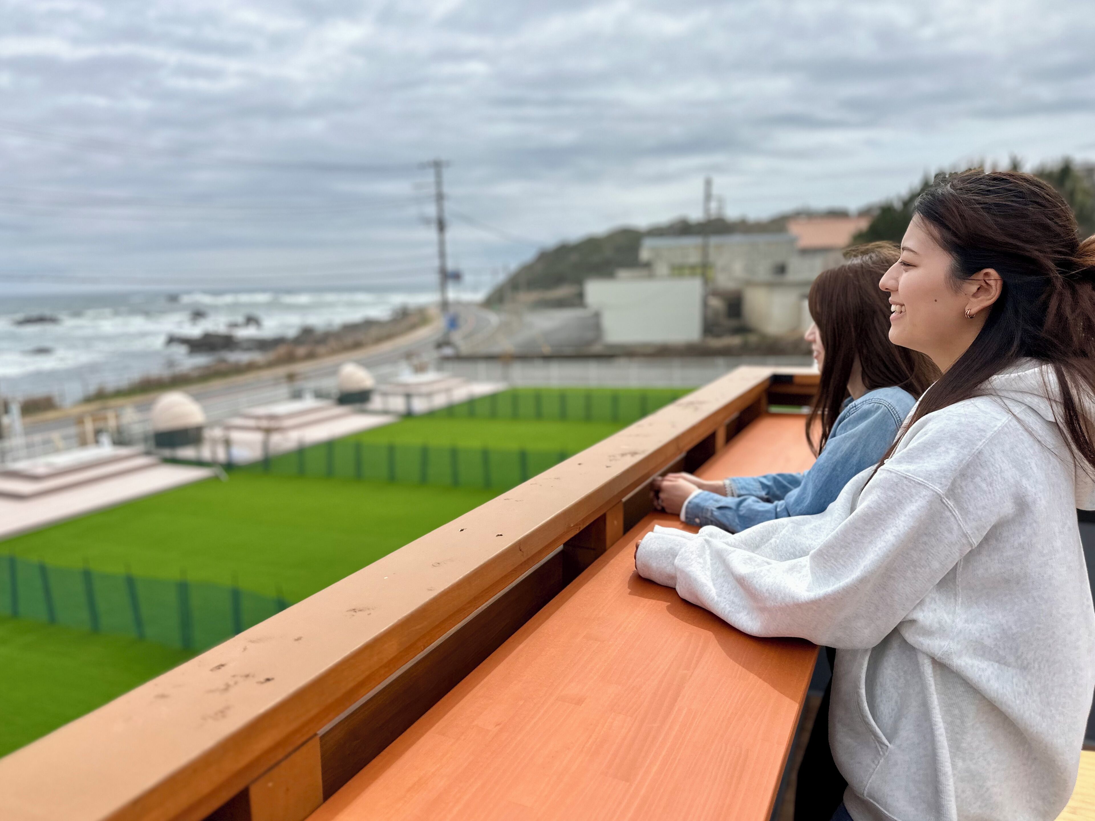 Vista da un balcone su un prato verde e sulla costa, con edifici e una strada.