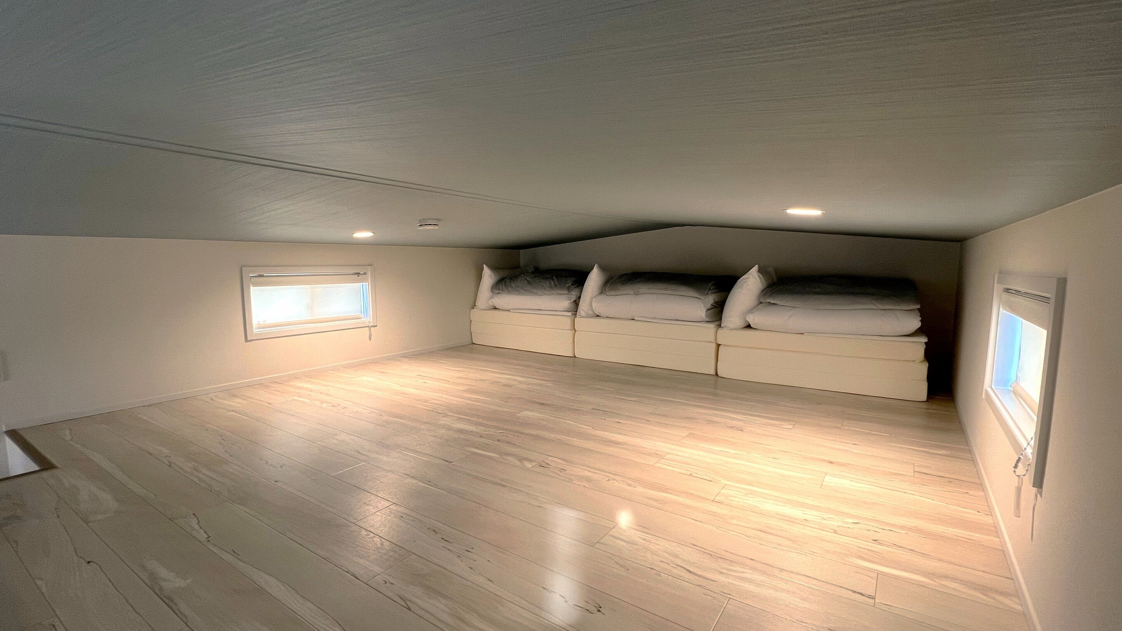 A small attic bedroom with a sloped ceiling, wooden flooring, and a built-in bed with pillows.