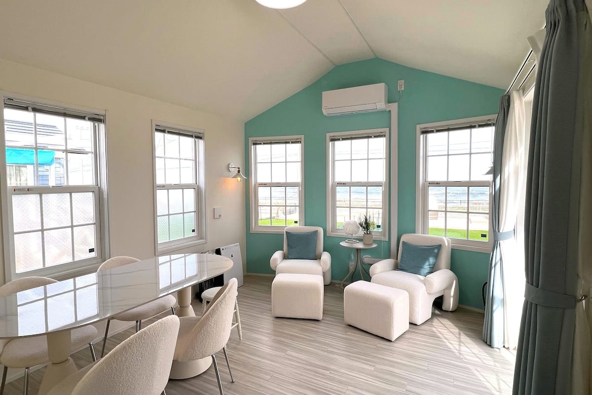 Una habitación amplia con una mesa de comedor y sillas, ventanas grandes con cortinas y una pared de acento color turquesa.