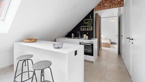 A modern kitchen with white cabinetry, a brick accent wall, and a small island with stools. - BARN - Waasmunster (Waasmunster)