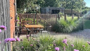 A rustic outdoor seating area with a wooden table and chairs, surrounded by a wooden fence and lush greenery. - BARN - Waasmunster (Waasmunster)