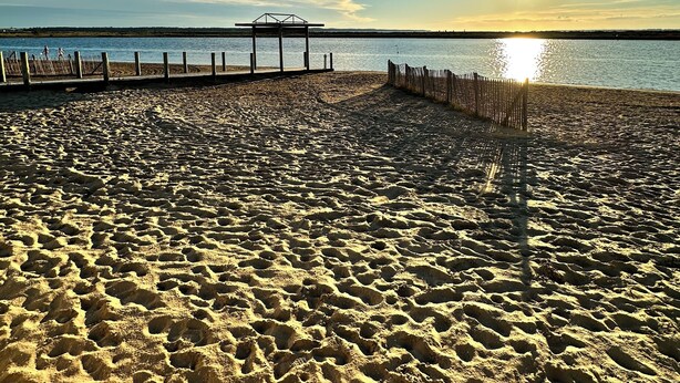 Una platja amb un moll de fusta i una zona tancada.
