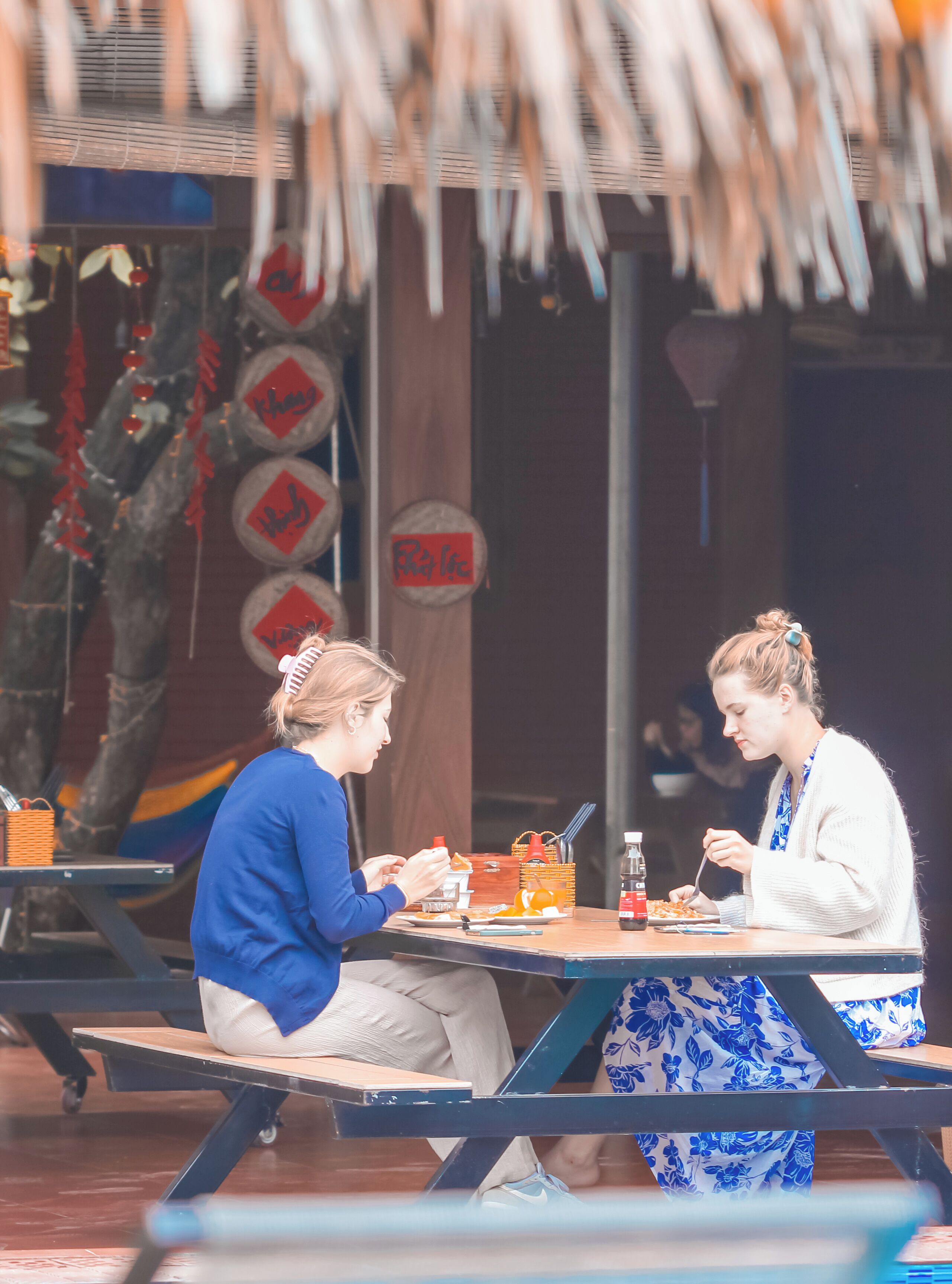 Two people dining at an outdoor table with a basket and a bottle of sauce.
