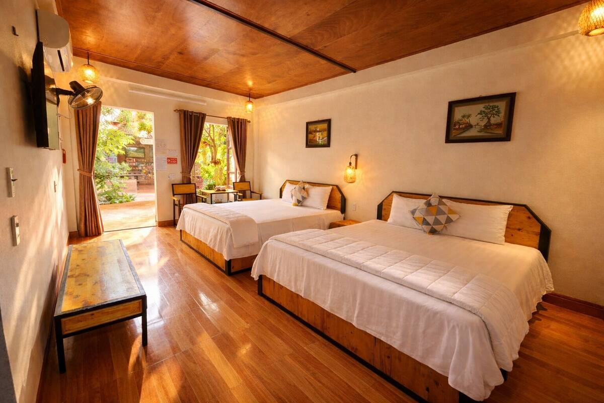 Habitación de hotel con dos camas, suelo de madera, una mesita y vistas a zonas verdes.