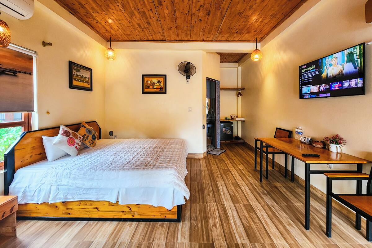 Una habitación con cama, televisión, mesa de comedor y techo de madera.