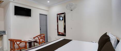 A hotel room with a bed, a TV mounted on the wall, a mirror, and a small table with chairs.