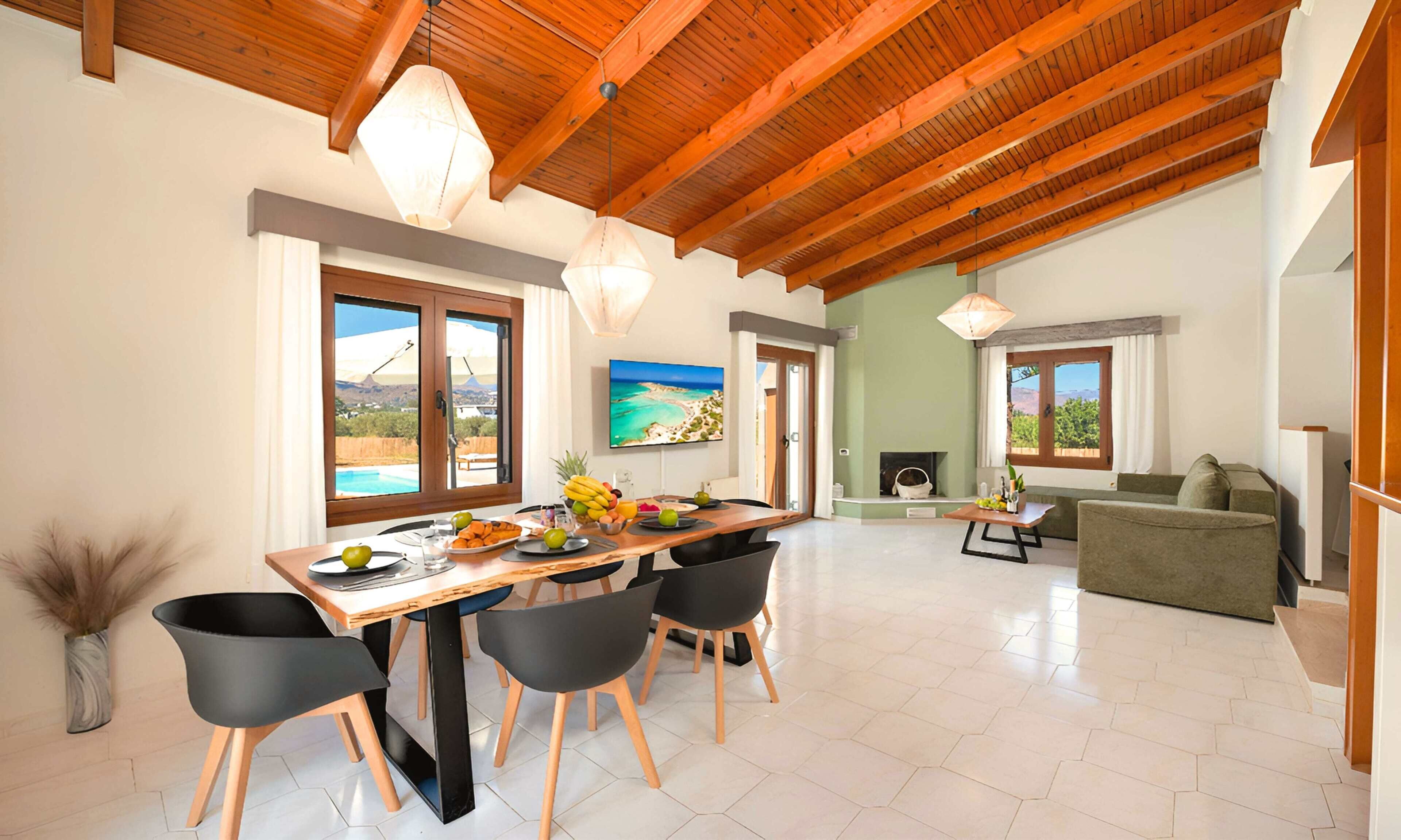 A spacious living area with a wooden ceiling, a dining table with chairs, a sofa, and a fireplace.