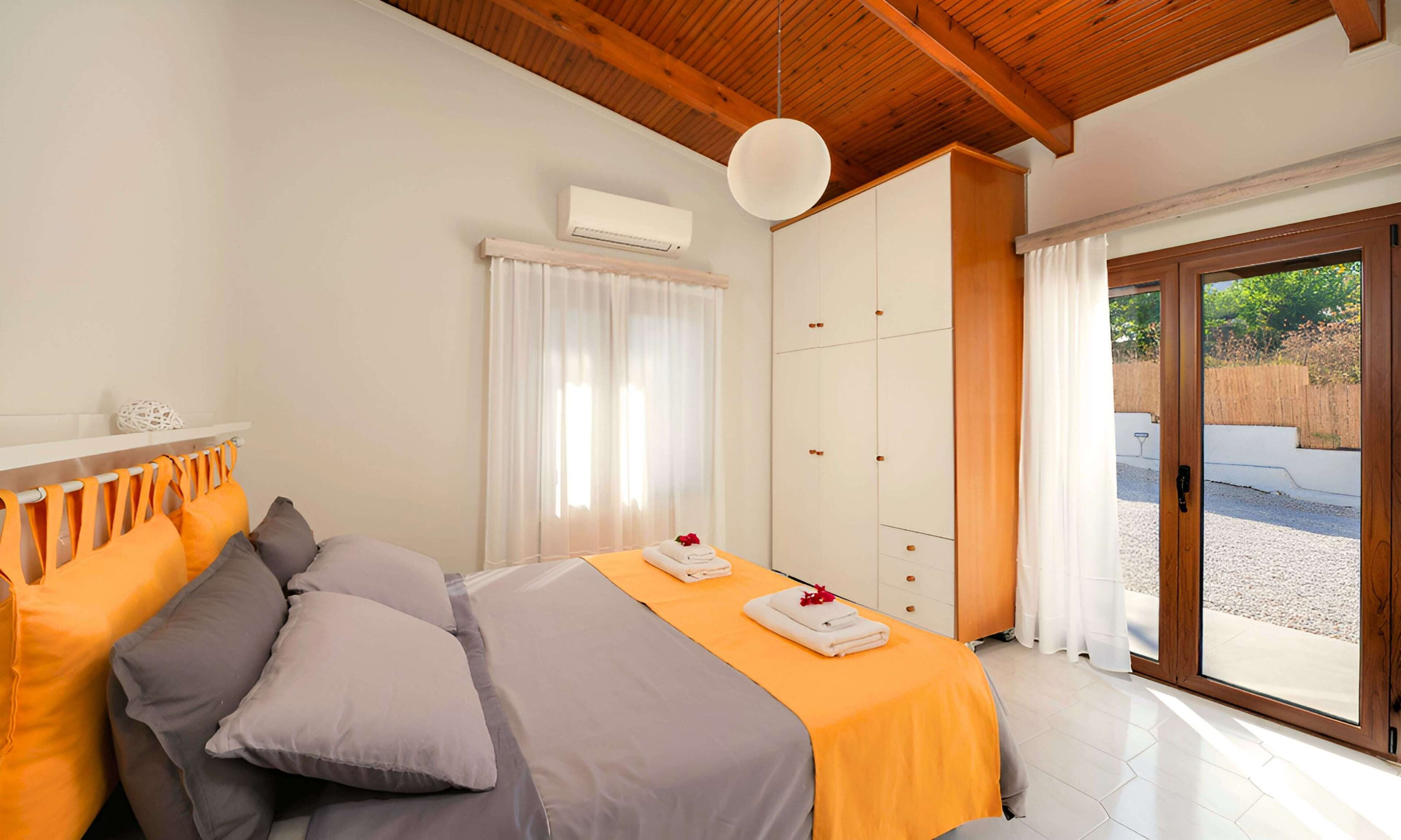 Quarto com cama, almofadas, guarda-roupa e porta de vidro deslizante para área externa.