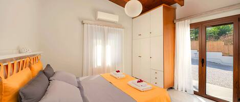 Quarto com cama, almofadas, guarda-roupa e porta de vidro deslizante para área externa.