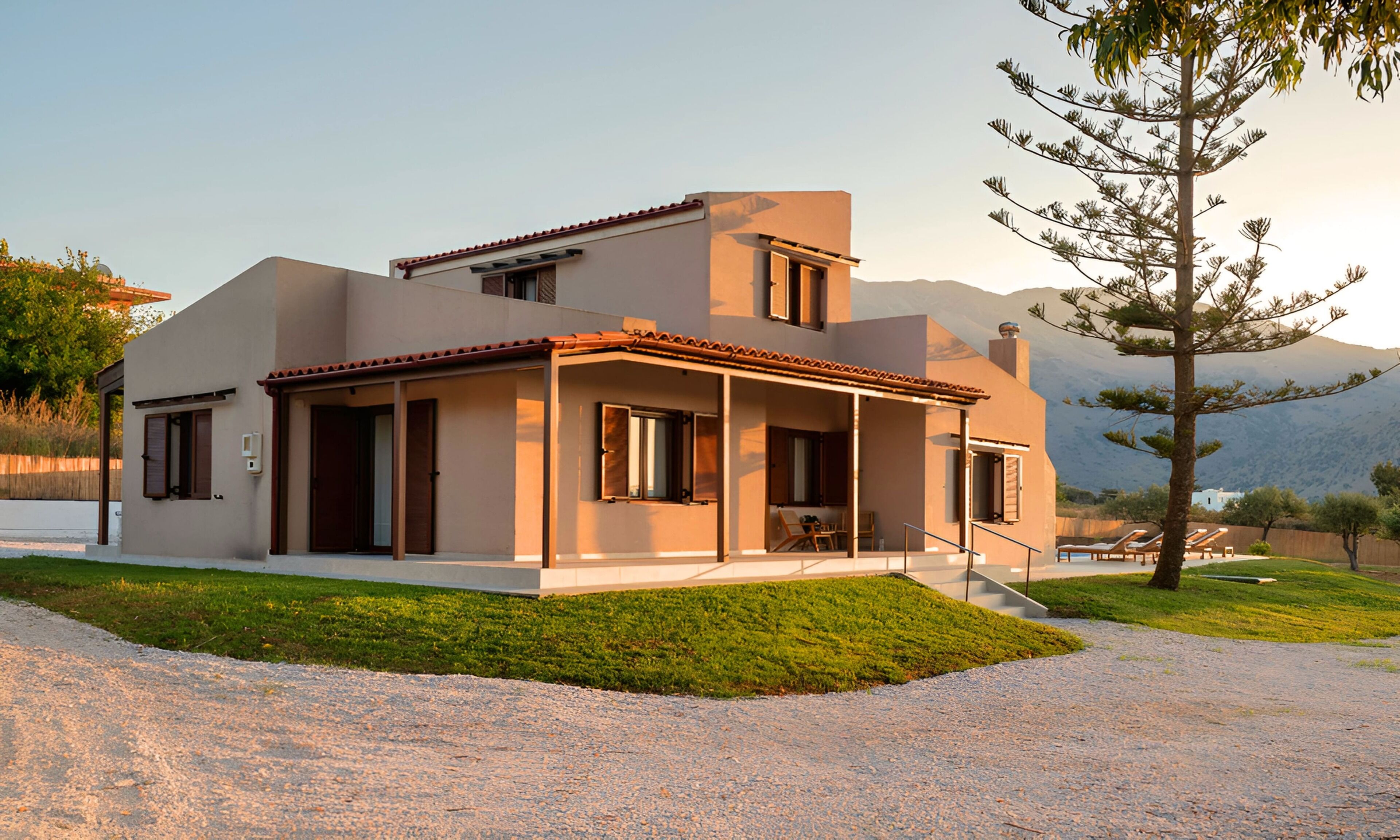 A modern two-story house with a covered patio and a view of mountains in the background.