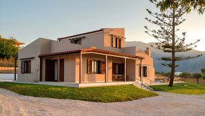 A modern two-story house with a covered patio and a view of mountains in the background. - Vegghera Villa Private Pool (Paralia Kourna)