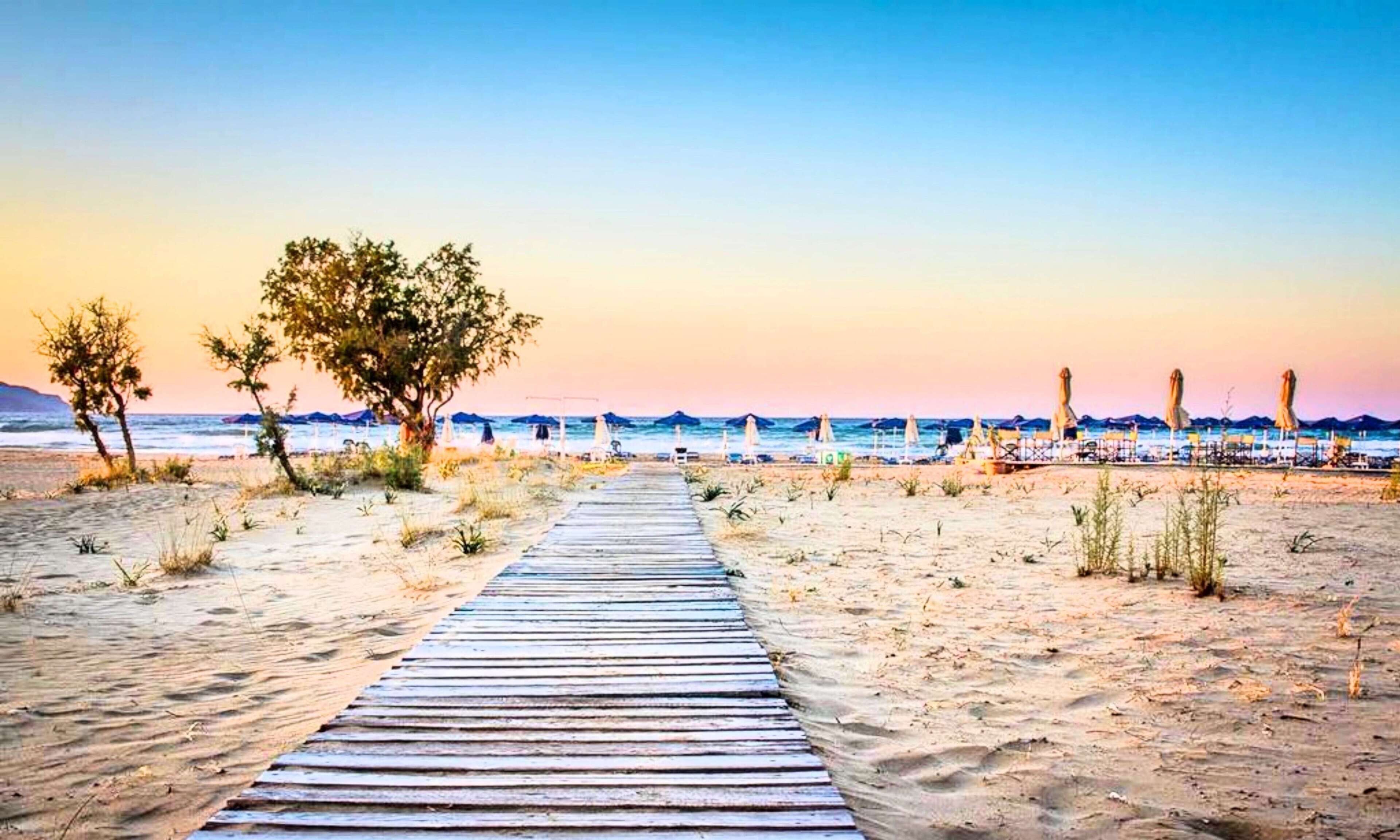 A wooden pathway leading to a beach with umbrellas and a clear view of the ocean.