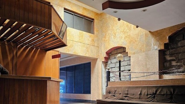 A spacious lobby with a central circular floor design, a wooden reception desk, a seating area with a sofa, and a stone fireplace. - Asis Hotel Eldoret  (Eldoret)