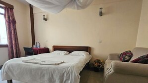 A hotel room with a bed, a chair, a sofa, a rug, and a window with curtains. - Asis Hotel Eldoret  (Eldoret)