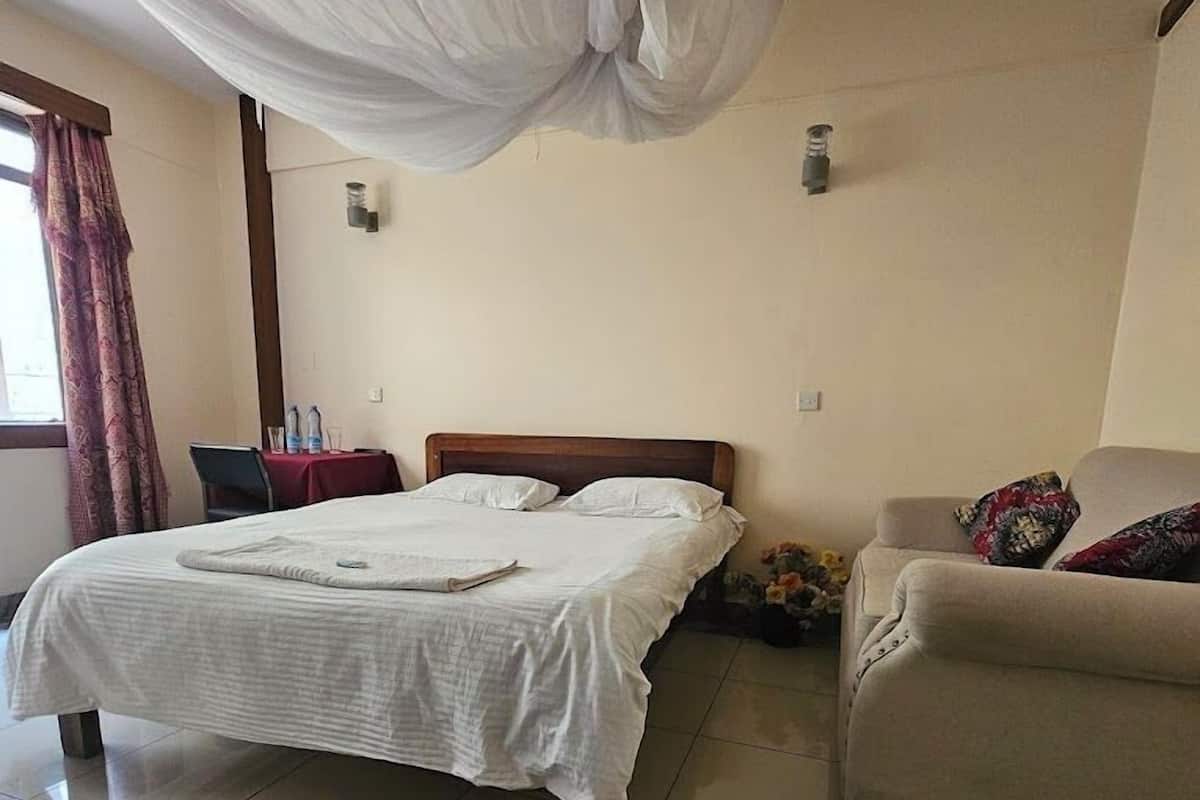 Una habitación de hotel con una cama, una silla, un sofá, una alfombra y una ventana con cortinas.