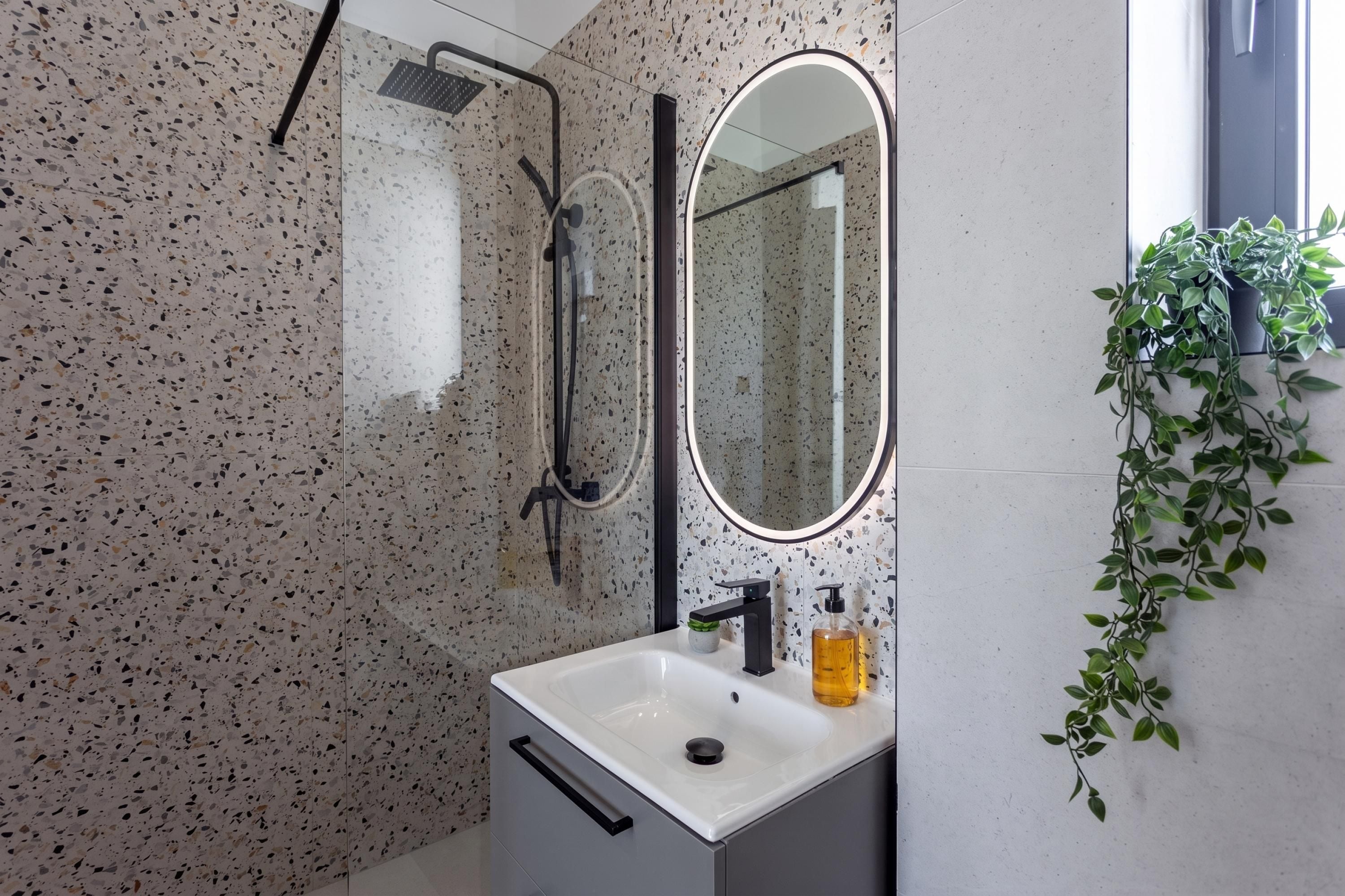 A bathroom with a freestanding bathtub, a mirror, a sink with a soap dispenser, and a potted plant.