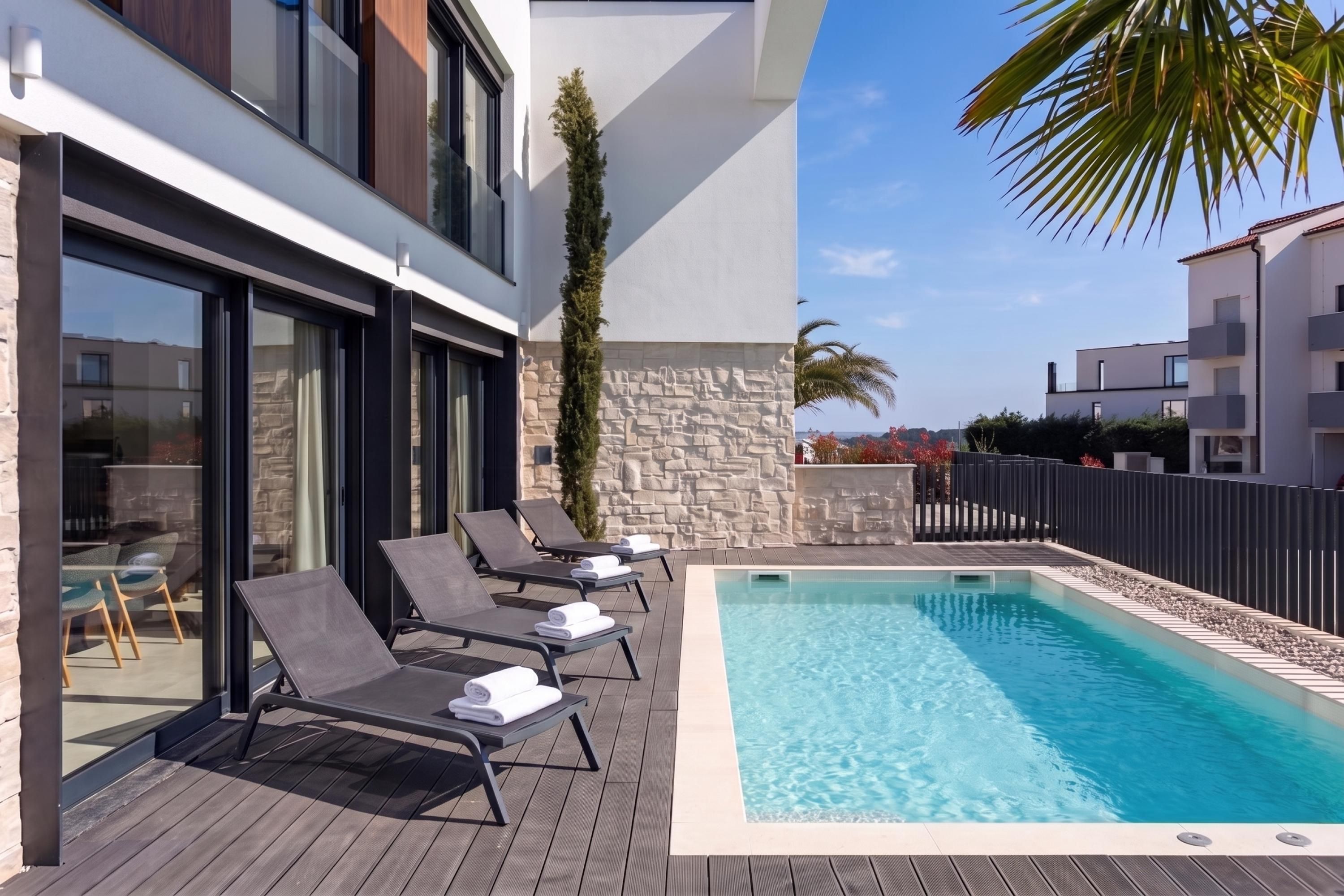 A modern outdoor pool area with lounge chairs and a stone wall.
