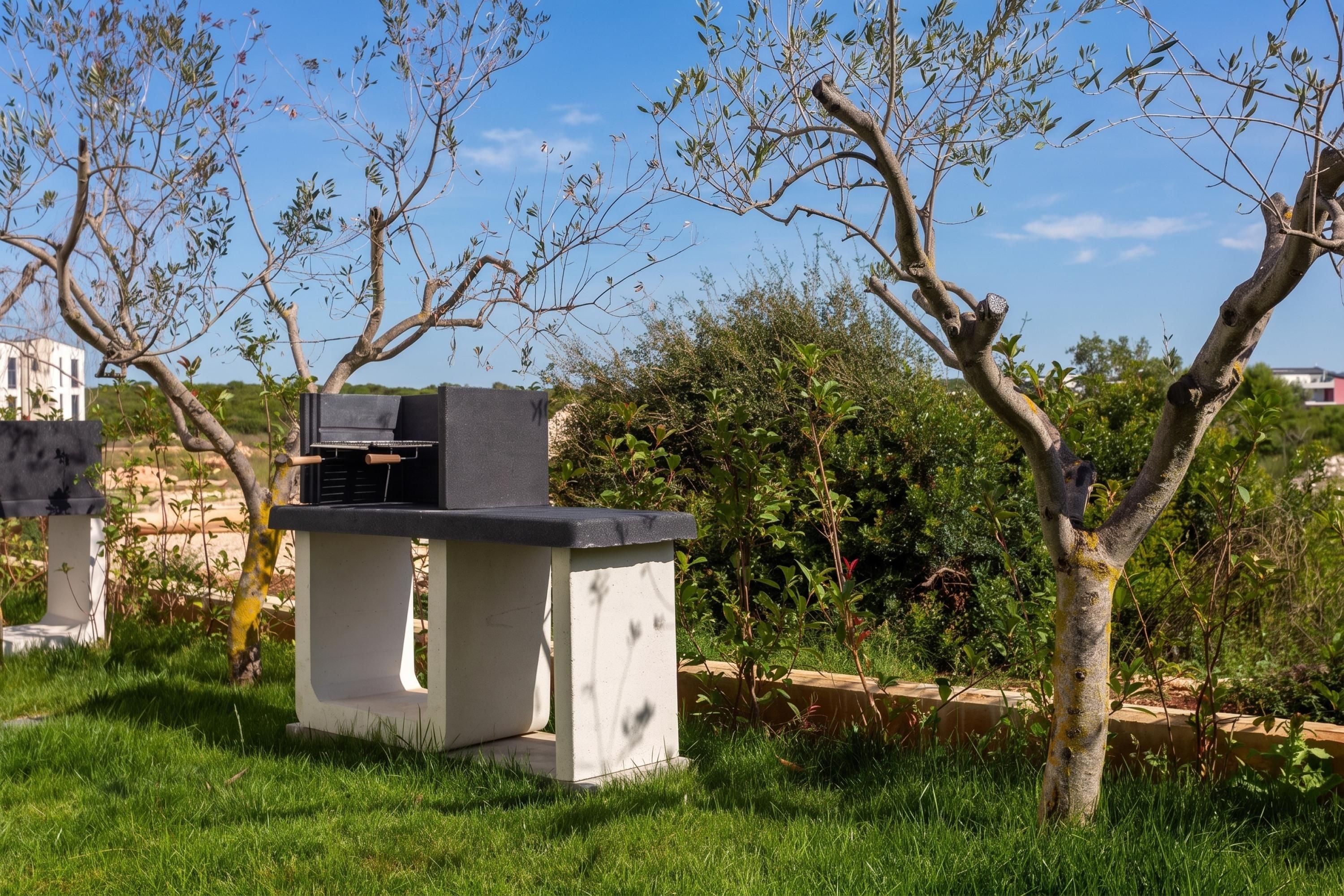 Una parrilla de hormigón exterior con chimenea, rodeada de césped y árboles.