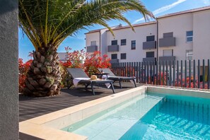 A pool area with lounge chairs, a palm tree, and a building in the background. - Villa Emma With Pool and sea view (Medulin)