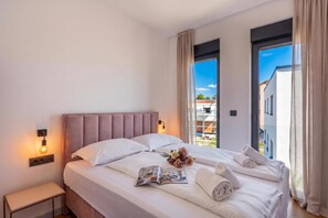 A hotel room with a large bed, a bedside table, a window with curtains, and a view of the outside. - Villa Emma With Pool and sea view (Medulin)