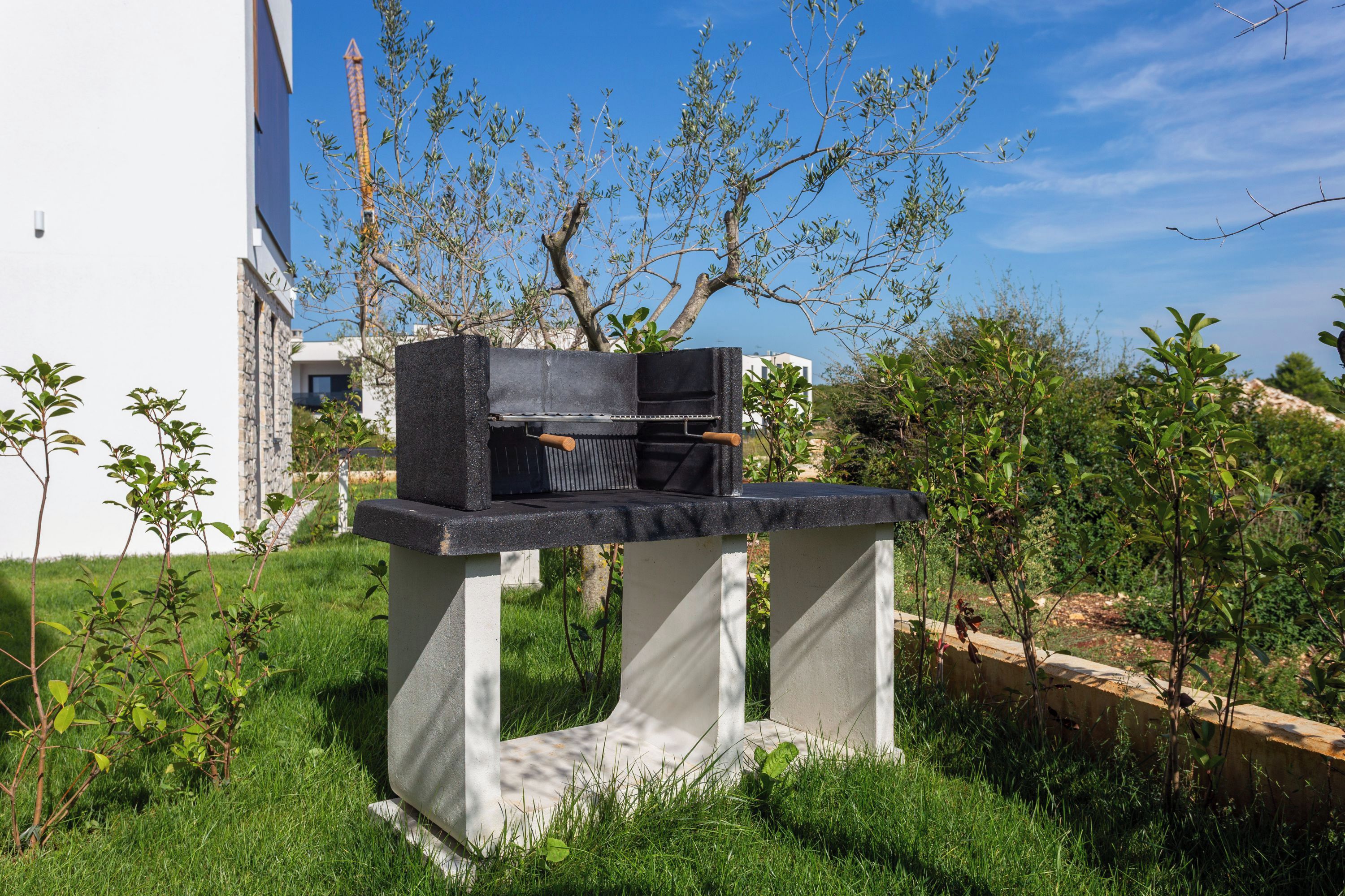 Una moderna instalación de parrilla al aire libre sobre una plataforma de hormigón en un jardín ajardinado.