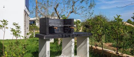 Una moderna instalación de parrilla al aire libre sobre una plataforma de hormigón en un jardín ajardinado.