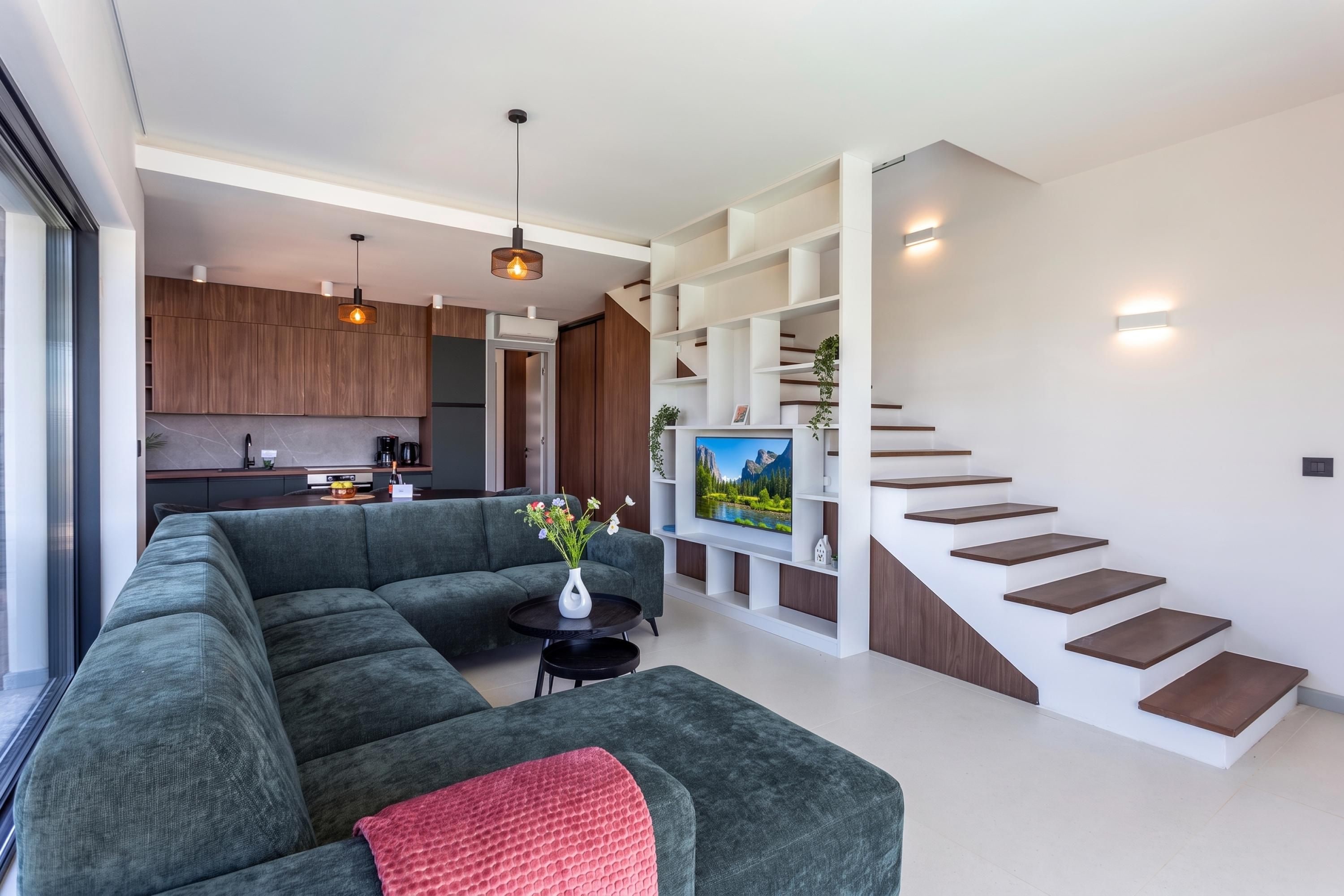 A modern living space with a sectional sofa, a dining area, a kitchen, and a staircase.