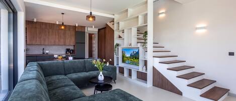 A modern living space with a sectional sofa, a dining area, a kitchen, and a staircase.