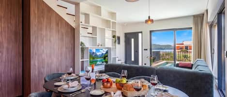 A dining area with a table set for four, a sofa, and a TV displaying a mountainous landscape.