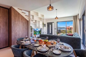 A dining area with a table set for four, a sofa, and a TV displaying a mountainous landscape. - Villa Petra with Pool and Sea View (Medulin)