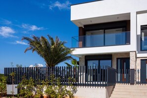 Una casa moderna de dos pisos con un balcón, una palmera y una cerca.