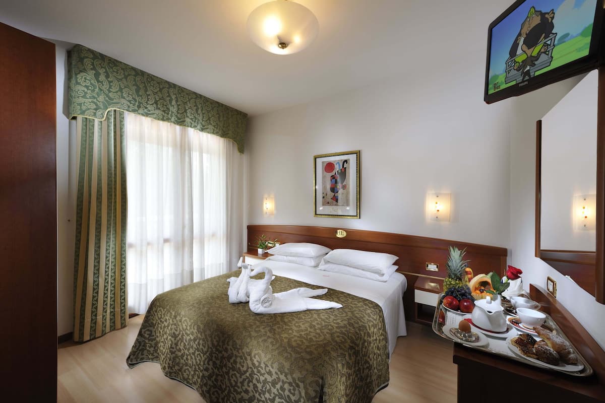 Hotelkamer met een bed, nachtkastje met een ontbijttafel, een televisie en een schilderij aan de muur.