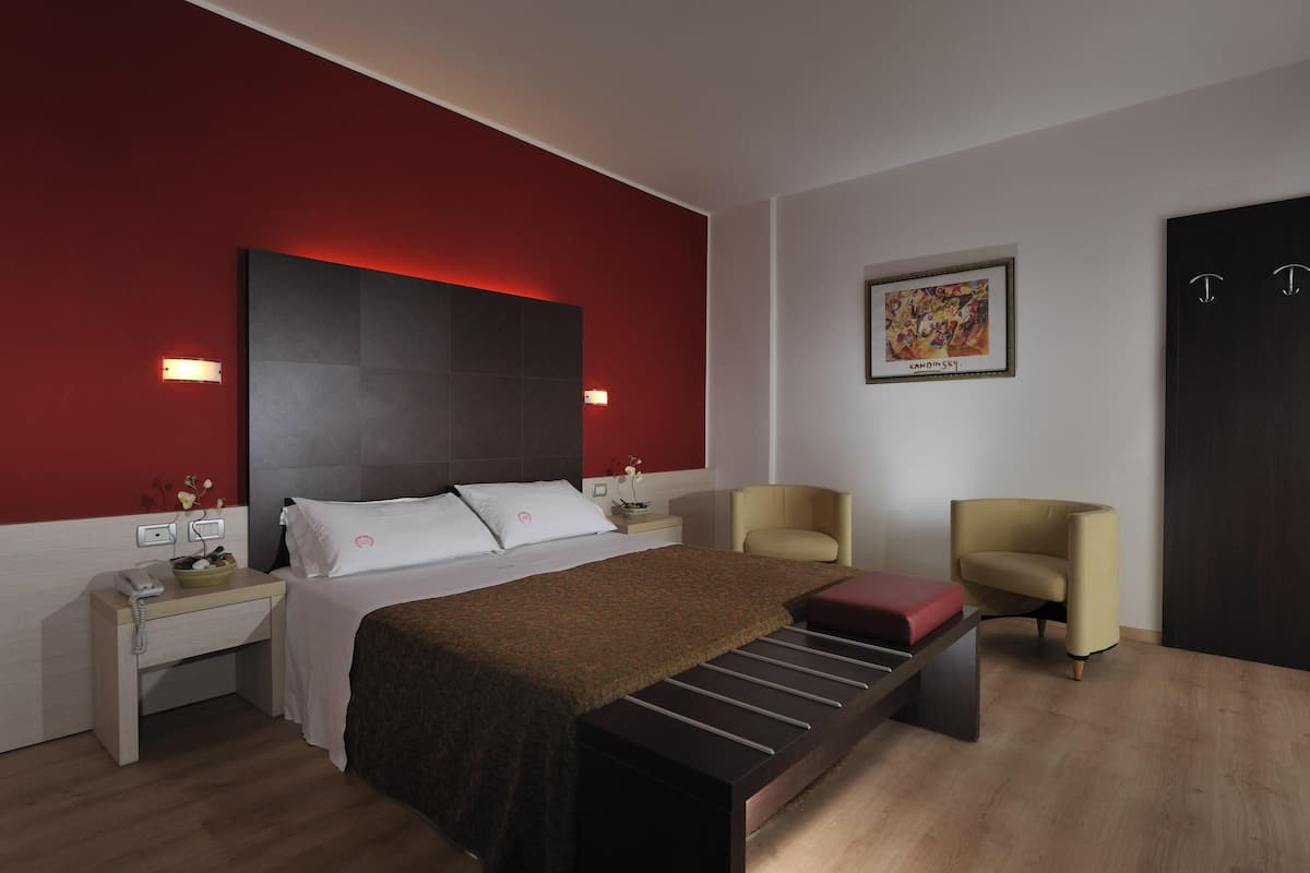 Een moderne hotelkamer met een groot bed, nachtkastjes, een bureau, twee stoelen en een schilderij aan de muur.